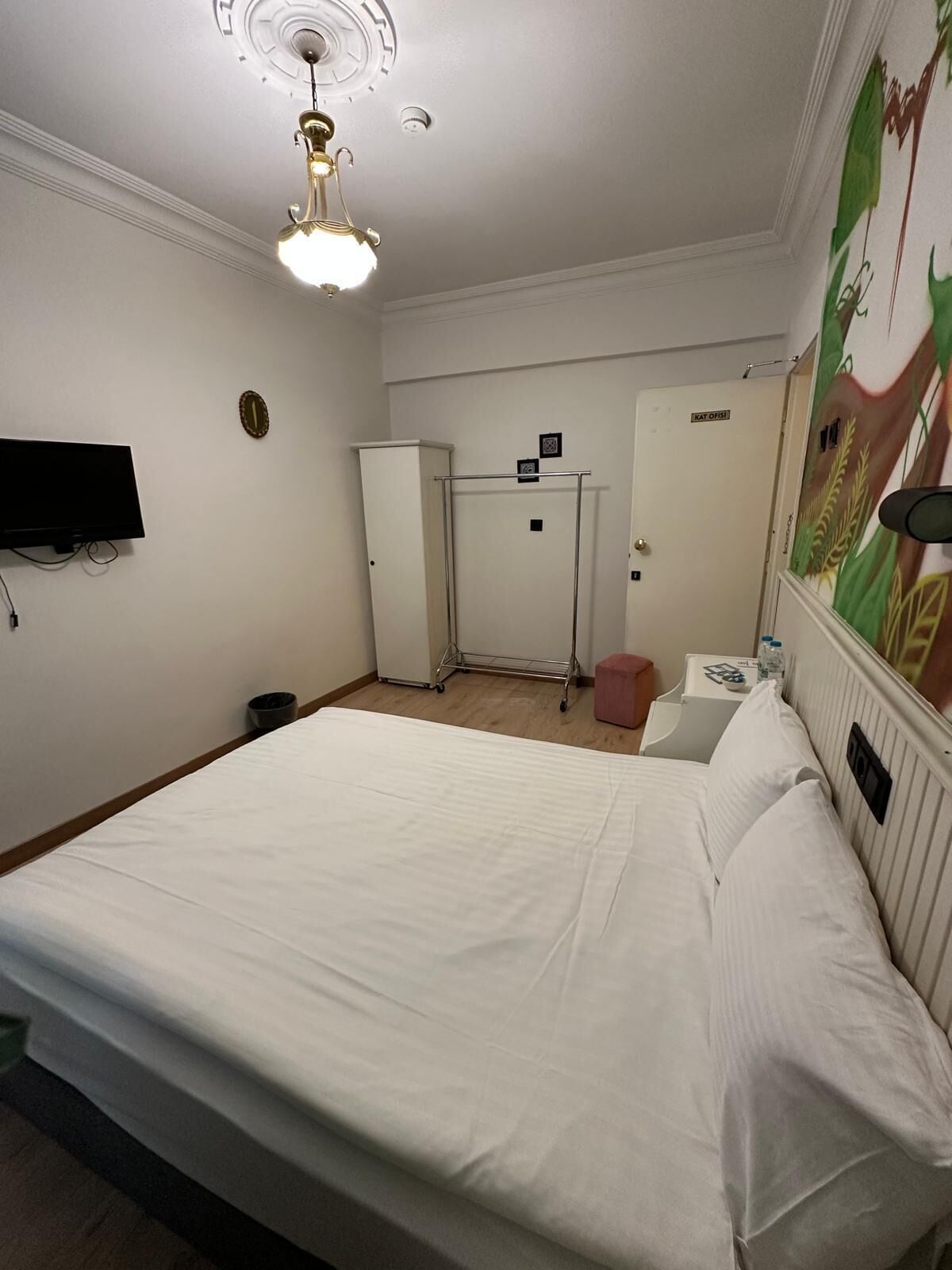 A hotel room with a bed, a desk, a chair, a television, a wardrobe, a mirror, and a ceiling fan.