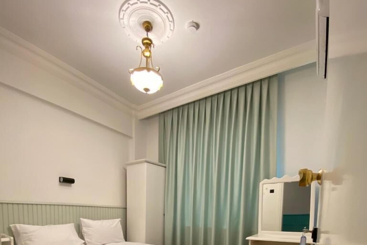 A bedroom with a bed, a nightstand, a dresser, a mirror, and a window with curtains.