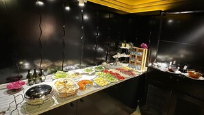Una mesa de buffet con diferentes alimentos y salsas, frente a una pared oscura con detalles amarillos en el techo.