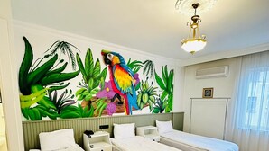 Habitación de hotel con tres camas individuales, un mural de un loro y plantas tropicales en la pared, y un ventilador de techo.