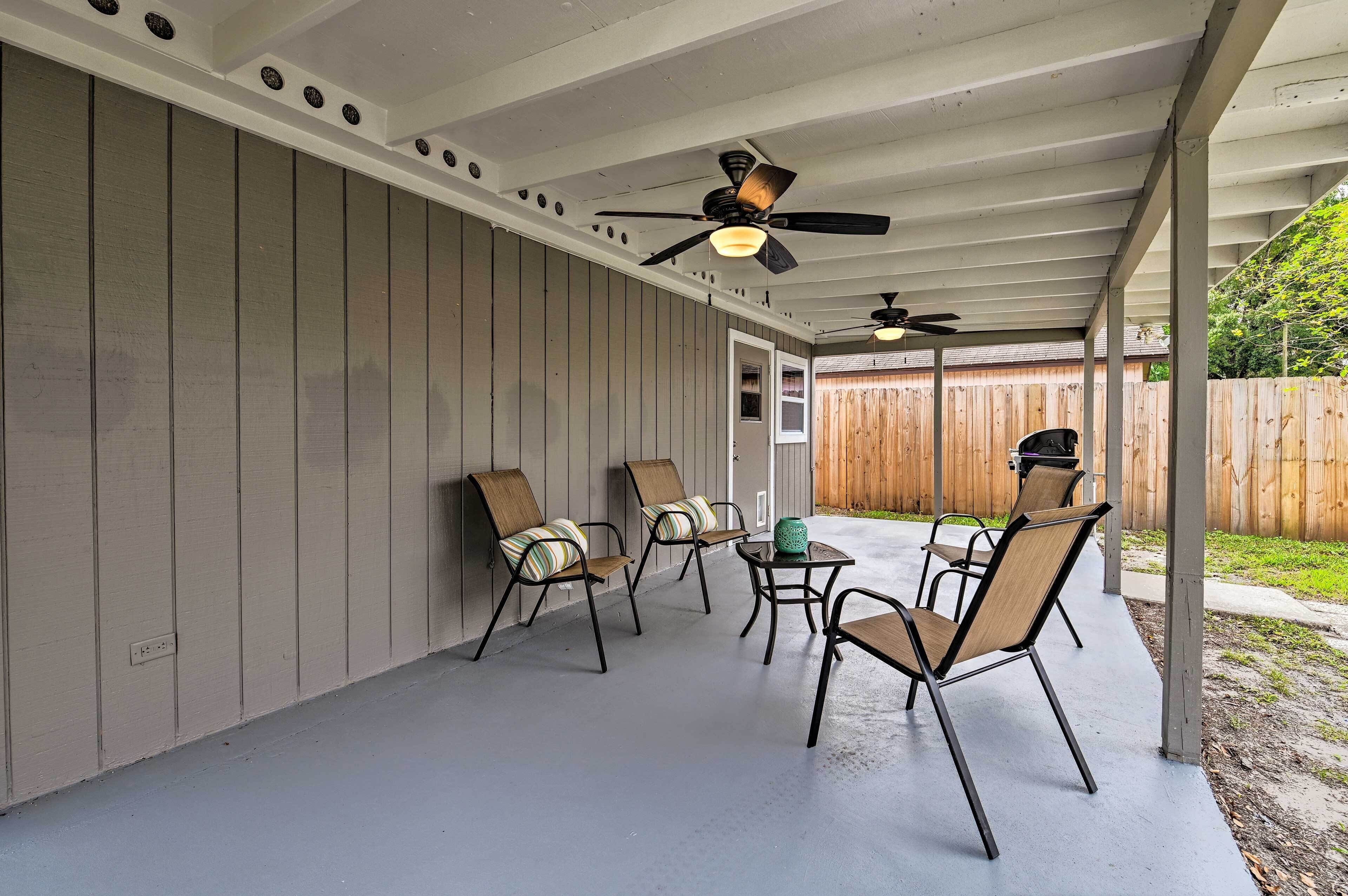 Un patio techado con ventiladores de techo, sillas de madera con cojines y una pequeña mesa.
