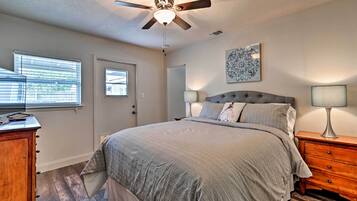 A bedroom with a bed, a ceiling fan, a nightstand, a lamp, a dresser, a door, and a window with blinds.
