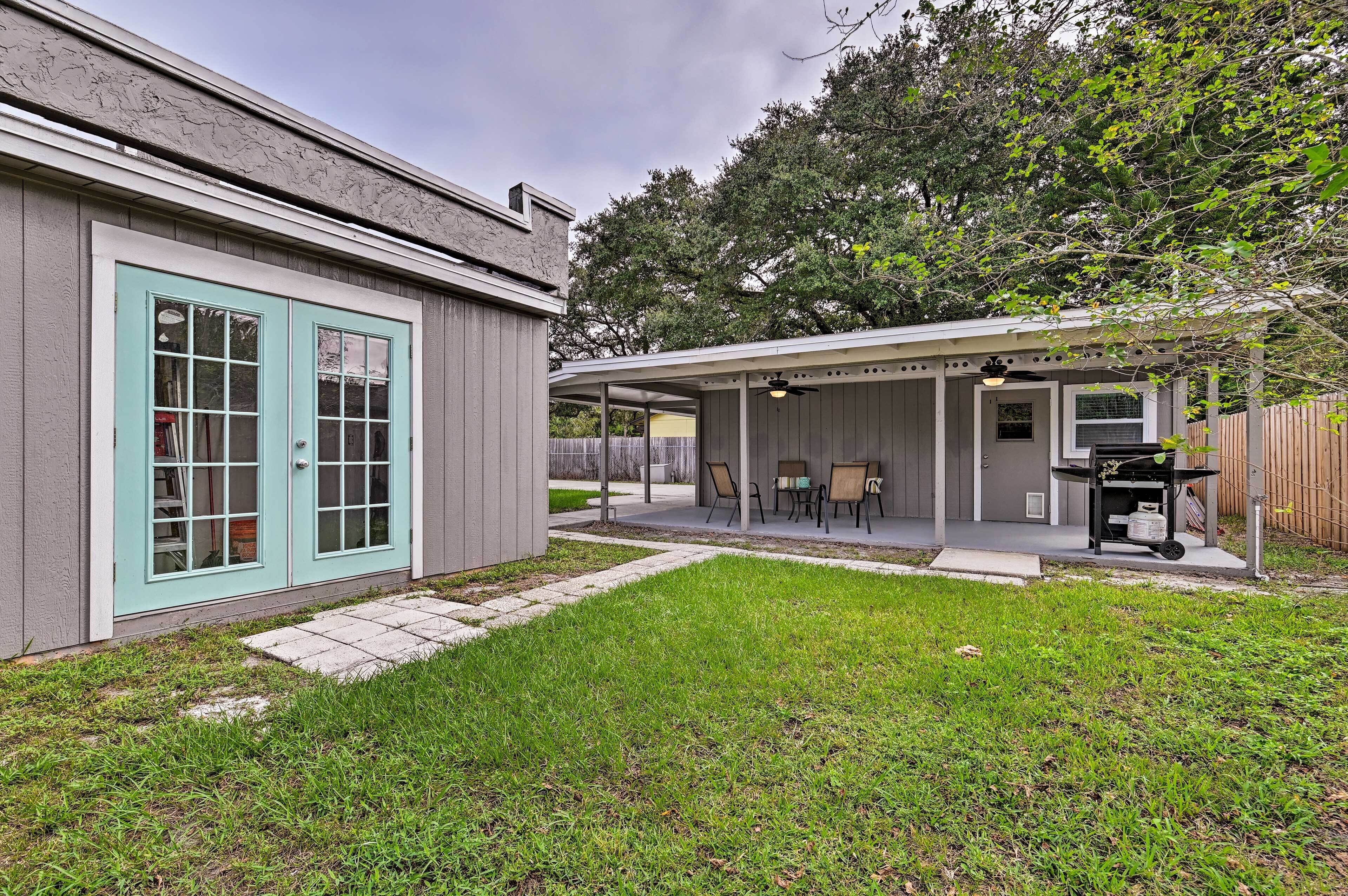 A backyard with a covered patio, a grill, and a small table with chairs.
