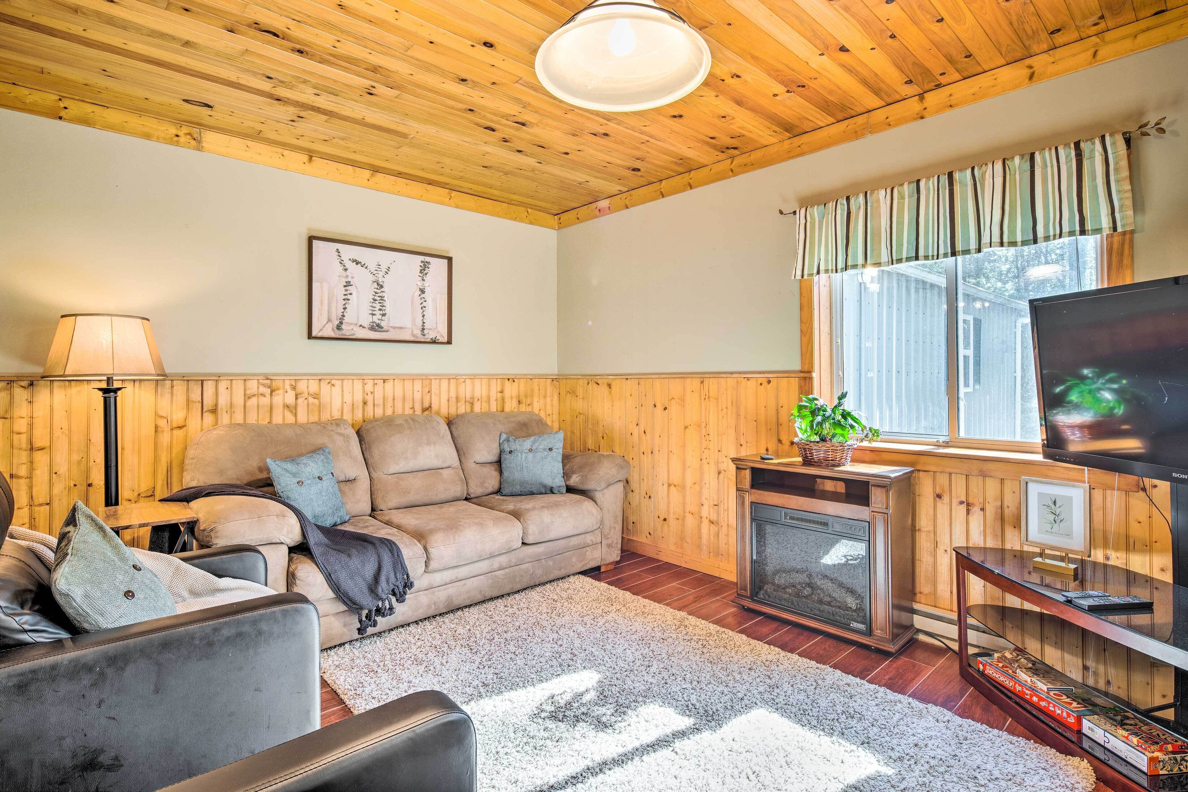 A cozy living room with a wooden ceiling, a beige sofa, a television, and a fireplace.