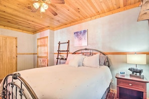 A bedroom with a wooden ceiling, a bed with white bedding, a nightstand with a lamp and a pig figurine, and a map on the wall. - Penrose Home w/ Covered Deck + Fire Pit! (Penrose)
