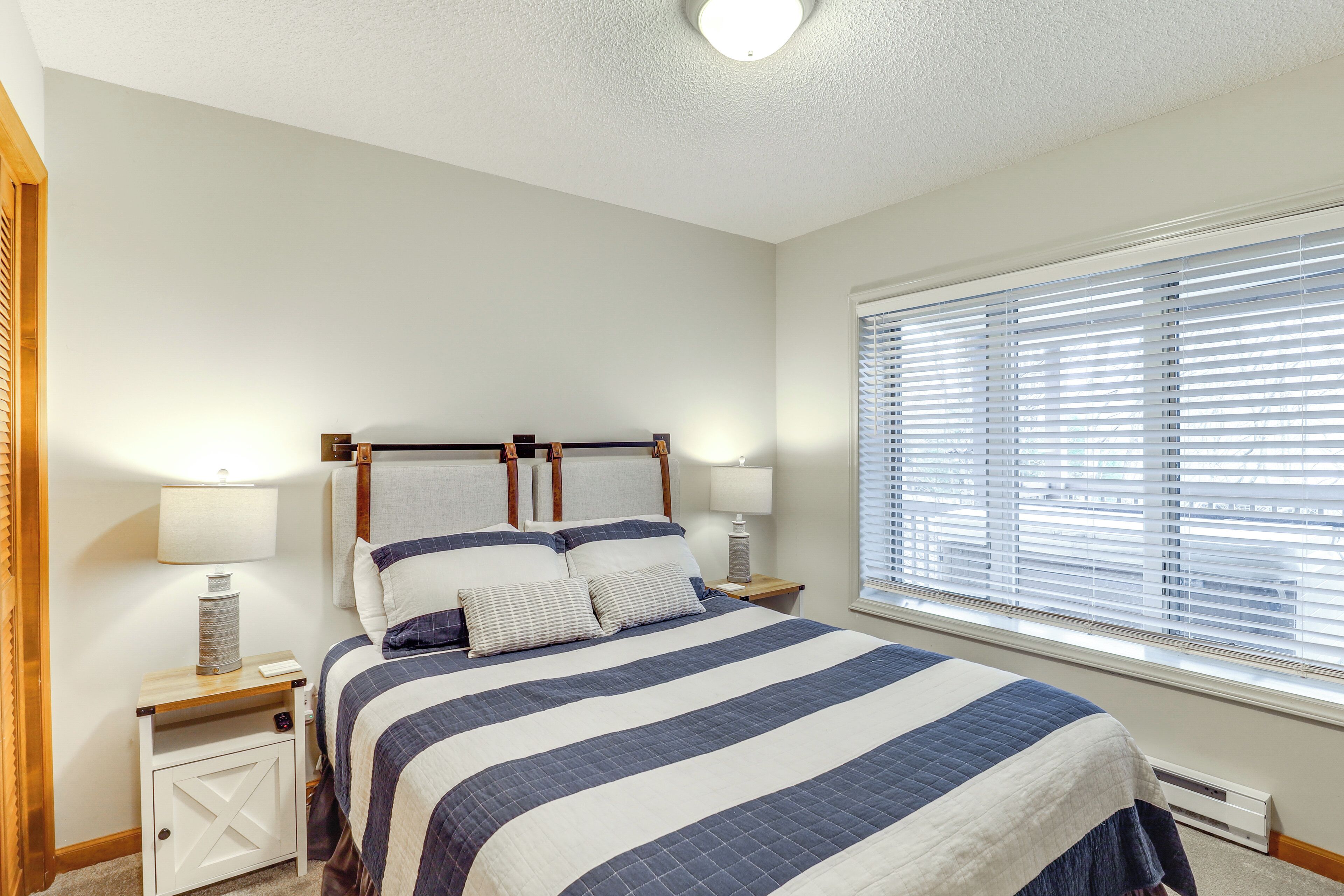 A bedroom with a bed, nightstands, lamps, and a window with blinds.