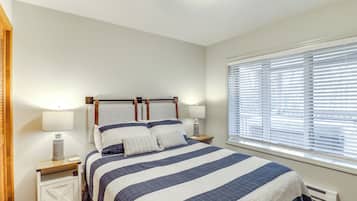 A bedroom with a bed, nightstands, lamps, and a window with blinds.