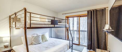 A bunk bed room with a window, a bedside table, and a lamp.