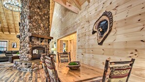 A rustic interior with a stone fireplace, wooden dining table, and chairs. - Riverfront Cabin w/ Hot Tub - 3 Miles to Dollywood (Pigeon Forge)