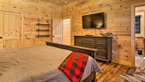 A wooden-paneled bedroom with a bed, dresser, and a ceiling fan. - Riverfront Cabin w/ Hot Tub - 3 Miles to Dollywood (Pigeon Forge)