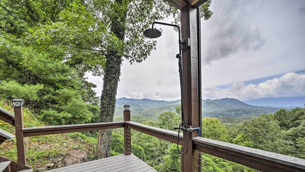 A wooden deck with a showerhead, overlooking a forested mountain landscape.