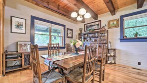 A wooden dining table with chairs, a chandelier, and a window with a view of trees.