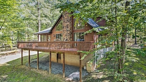 Una cabaña con terraza de madera, base de piedra y ventanas amplias.