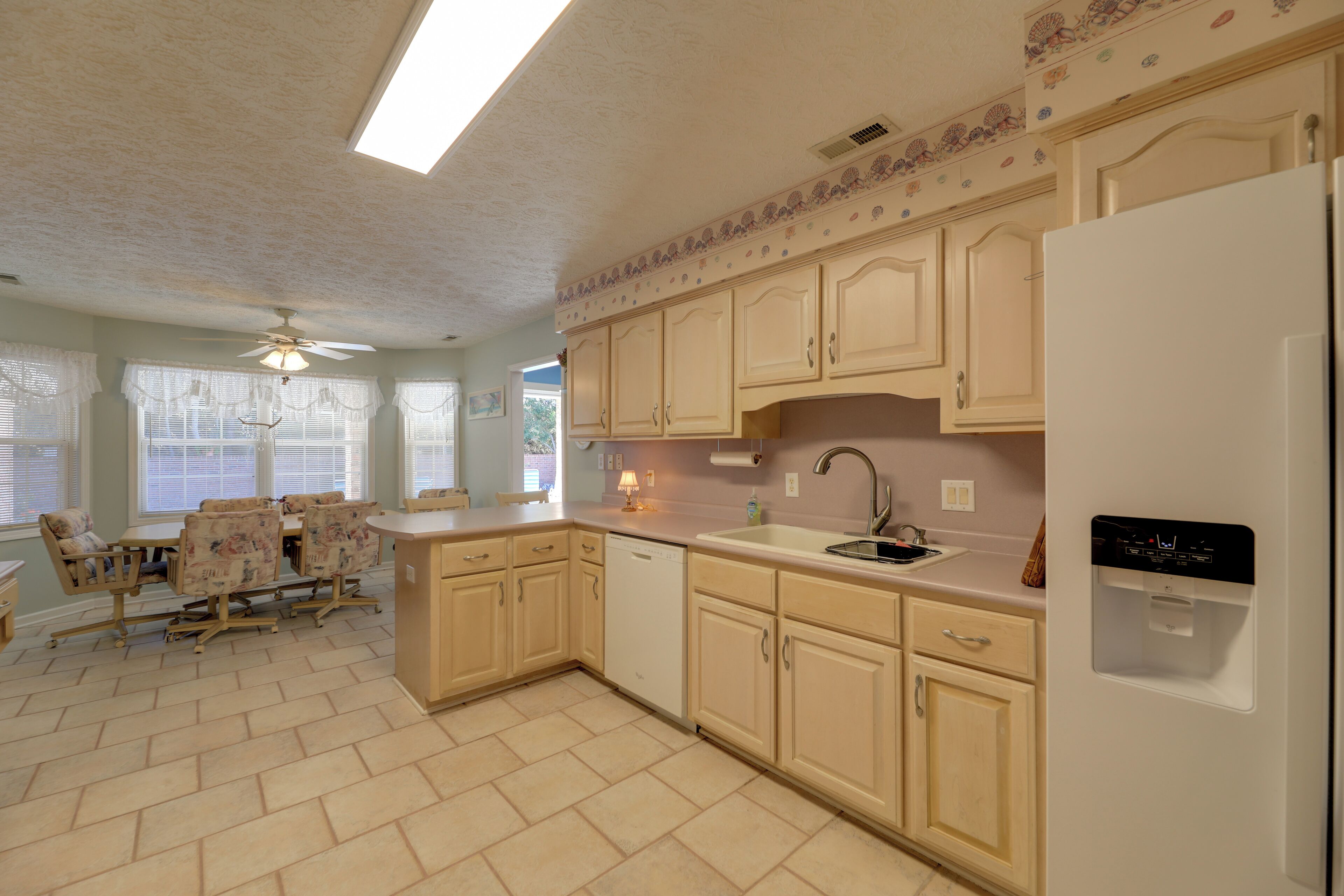A kitchen with light-colored cabinets, a dishwasher, a refrigerator, and a dining area with a table and chairs.