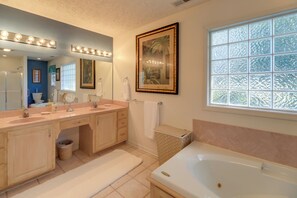 Ein Badezimmer mit doppelter Waschtisch, großem Spiegel mit Beleuchtung, einer Badewanne und einem Fenster mit Milchglas.