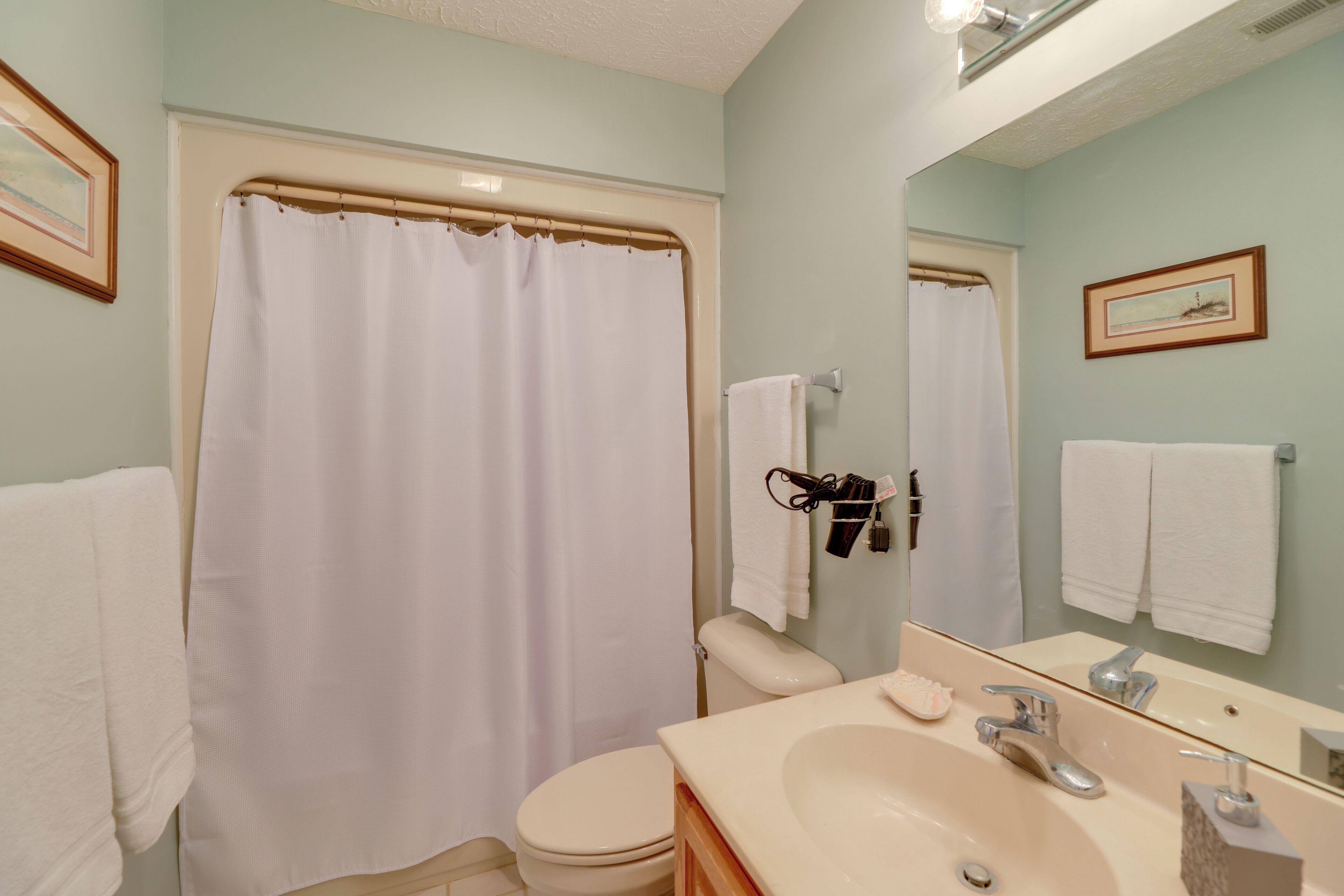 A bathroom with a shower curtain, toilet, sink, and mirror.