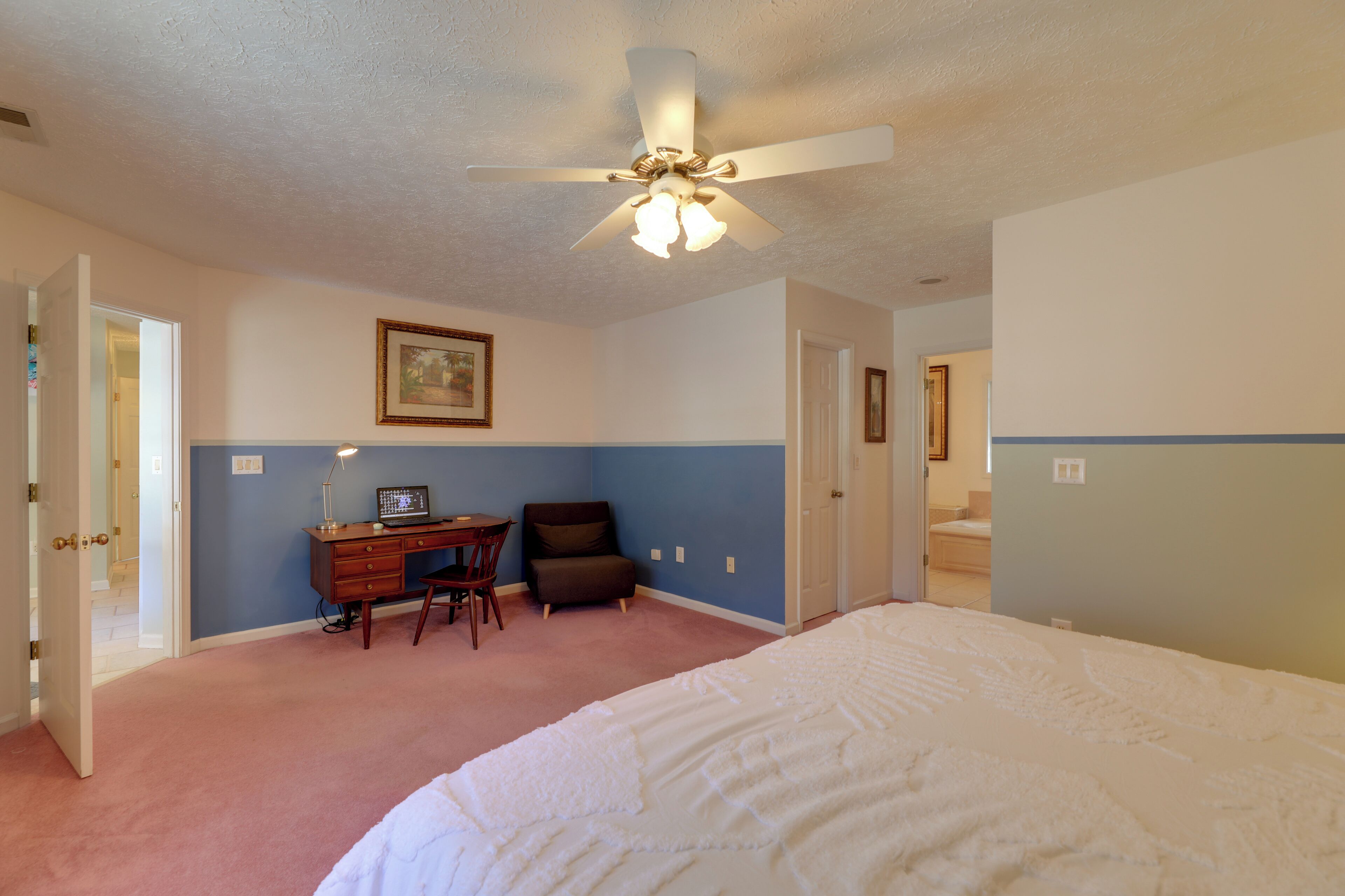 A bedroom with a bed, desk, chair, and a ceiling fan.