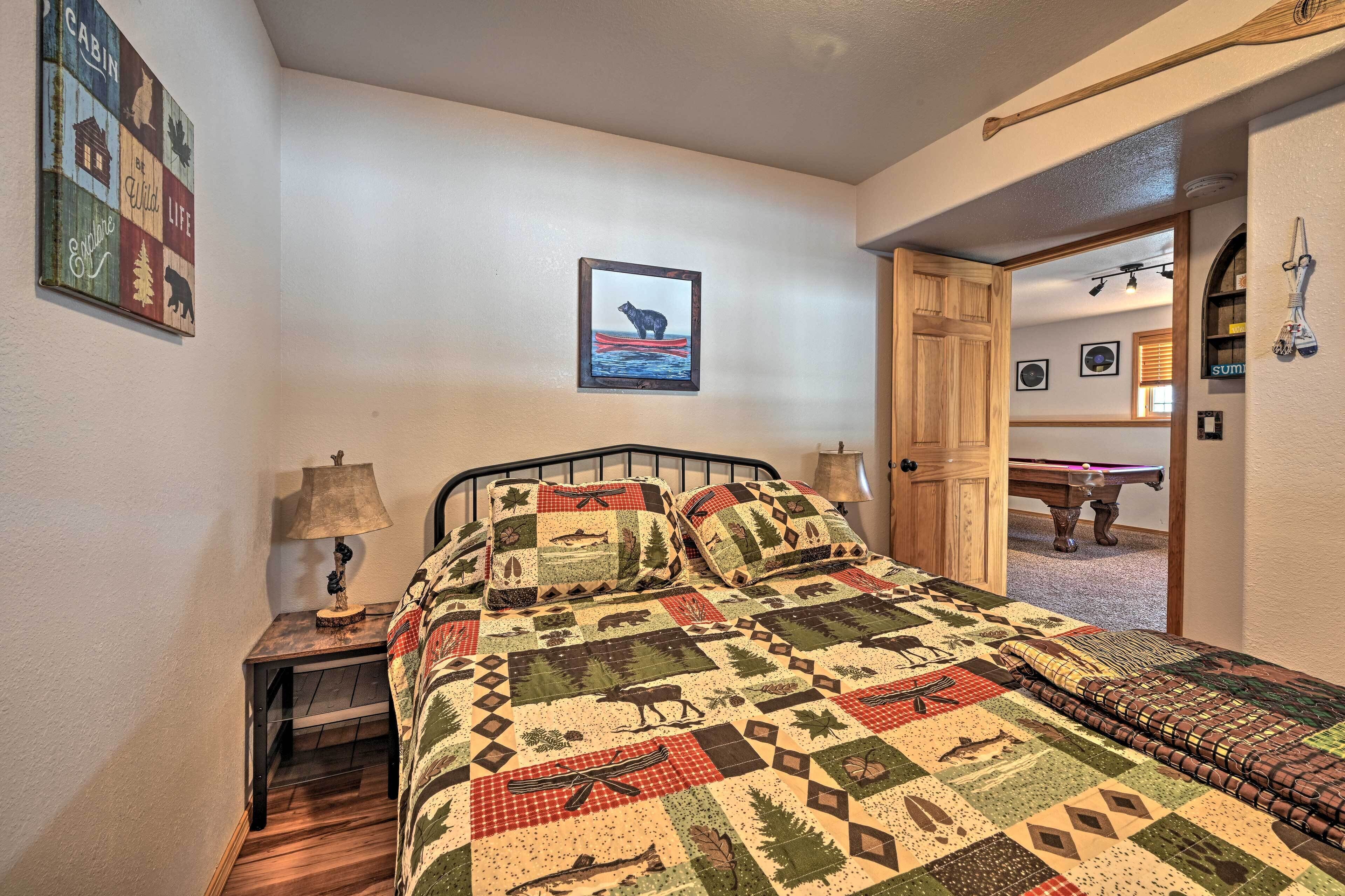Een slaapkamer met een bed, een nachtkastje, een lamp, een quilt met dierenmotieven, een lijst met een foto van een ijsbeer en een houten deur die naar een andere kamer leidt.