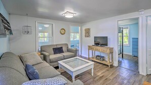 A living room with a sofa, a coffee table, a TV stand, and a clock on the wall. - NEW Cute & Charming Cottage Near Castle Rock Lake! (Friendship)