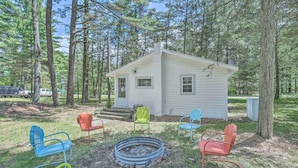 A small cabin with a fire pit surrounded by colorful chairs, set in a wooded area. - NEW Cute & Charming Cottage Near Castle Rock Lake! (Friendship)