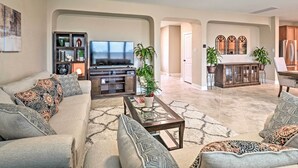 A spacious living room with a sofa, coffee table, and TV. There are potted plants and a cabinet with glass doors. - Texas Home w/ Patio & Grill ~ 16 Mi to Austin (Manor)