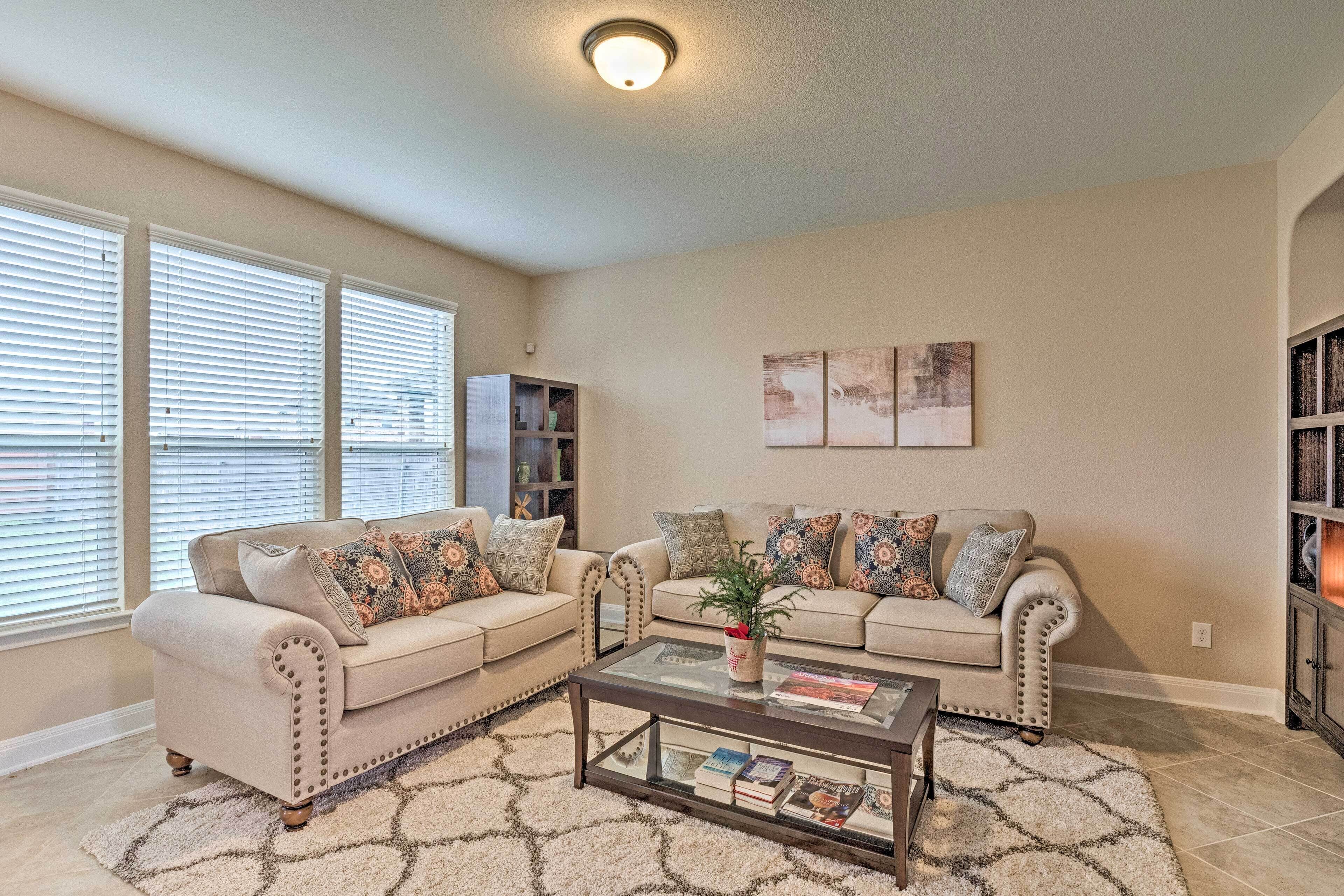 A living room with two beige sofas, a glass coffee table, and a patterned rug.