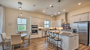 A modern kitchen with white cabinetry, stainless steel appliances, a central island with bar stools, and pendant lighting. - Luxury Ave Maria Rental w/ Private Pool & Spa! (Immokalee)