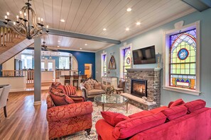 A spacious living room with a fireplace, red sofas, a glass coffee table, and a chandelier. - 16 Mi to Camelback Resort: Getaway w/ Game Room (Brodheadsville)