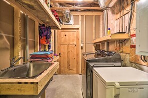A compact utility room with a sink, a washing machine, and a door leading to another room. - Quiet Riverside Retreat: Hike, Fish & Ski! (Eureka)