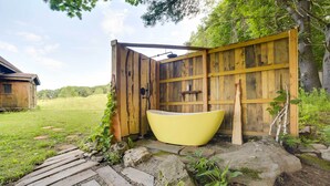 A rustic wooden outdoor shower area with a yellow bathtub, surrounded by natural stone and greenery. - Breathtaking Mtn Views: Stylish Rustic Retreat! (Bennington)