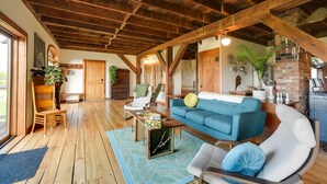 A spacious living room with wooden floors, a blue sofa, a white armchair, and a wooden coffee table. - Breathtaking Mtn Views: Stylish Rustic Retreat! (Bennington)