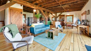 A spacious loft with exposed wooden beams, a blue sofa, a dining area, and a kitchen in the background. - Breathtaking Mtn Views: Stylish Rustic Retreat! (Bennington)