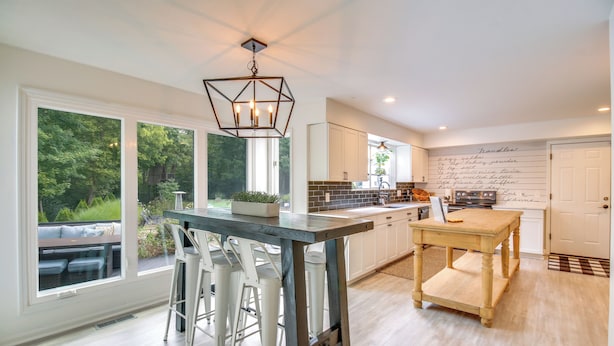 A modern kitchen with a large island, white bar stools, and a view of the outdoors. - Luxury Maineville Villa w/ Private Pool & Deck (Maineville)