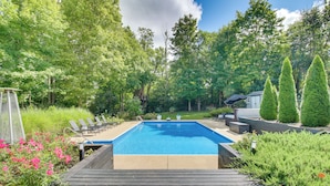 A rectangular swimming pool with a wooden deck in the foreground, surrounded by lush greenery and tall trees. - Luxury Maineville Villa w/ Private Pool & Deck (Maineville)