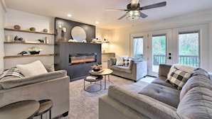 A modern living room with a fireplace, grey sofas, a coffee table, and a ceiling fan. - Luxury Maineville Villa w/ Private Pool & Deck (Maineville)