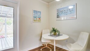Una habitación con una mesa redonda blanca, dos sillas blancas, una planta en maceta y obras de arte en las paredes.