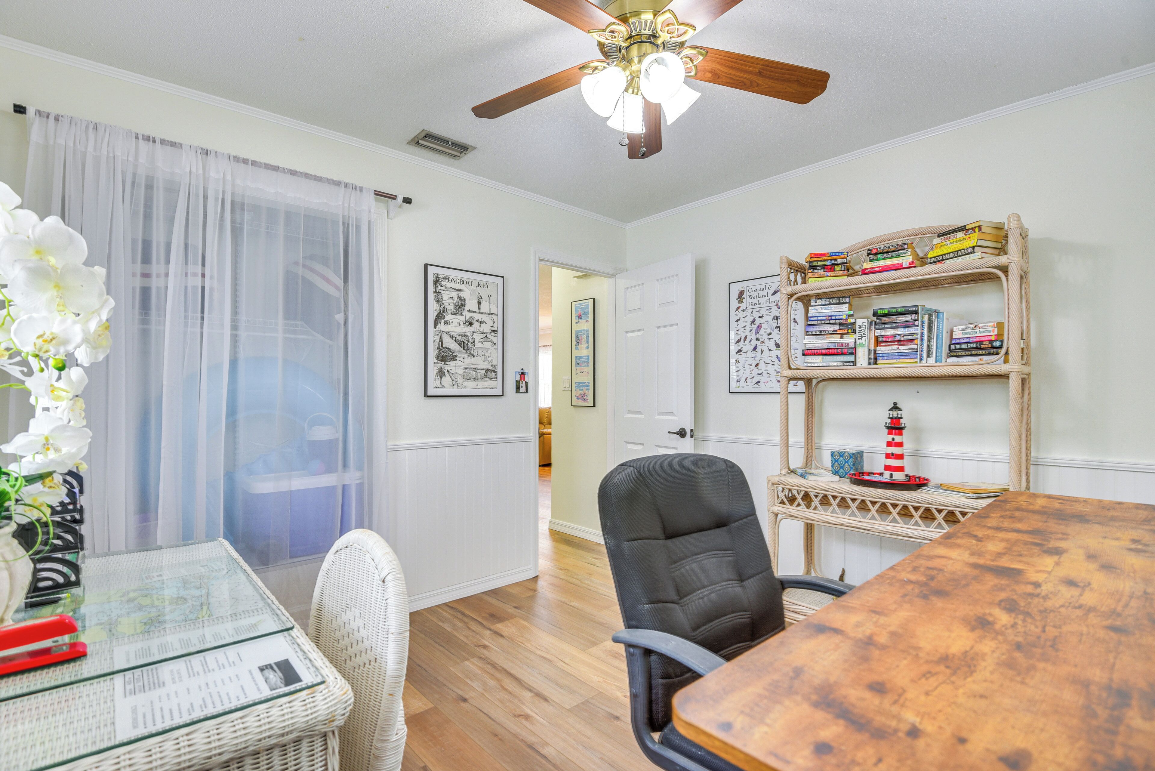 A dining area with a wooden table, chairs, a bookshelf, and a ceiling fan.