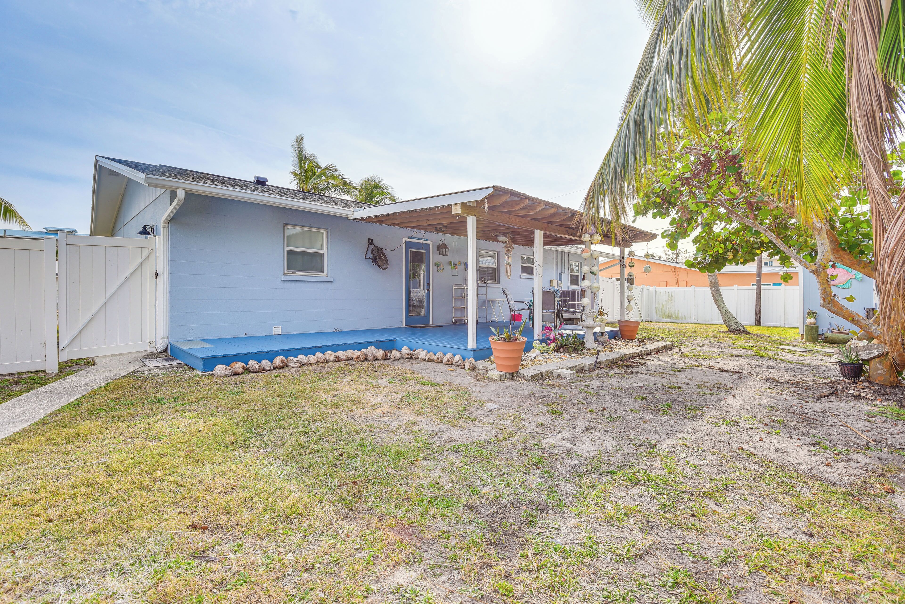 A single-story house with a blue exterior, a covered porch, and a small front yard with a palm tree.