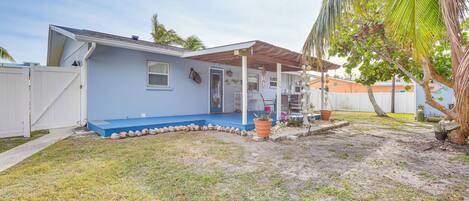A single-story house with a blue exterior, a covered porch, and a small front yard with a palm tree.