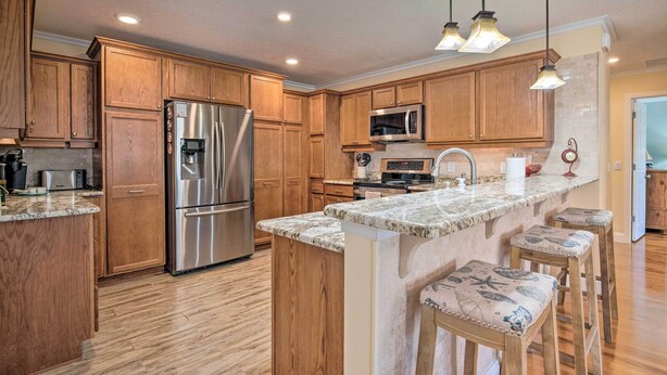 A kitchen with wooden cabinets, stainless steel appliances, a marble countertop, and bar stools. - ~ 1 Mi to Golf: Home w/ Patio in The Villages! (The Villages)