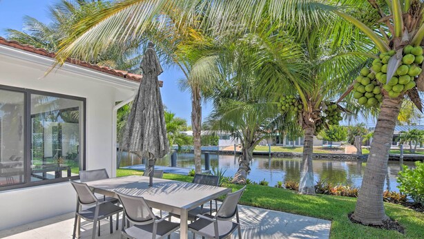 A modern outdoor dining area with a table and chairs, surrounded by palm trees and a water feature. - Luxe Wilton Manors Home w/ Private Boat Dock (Wilton Manors)