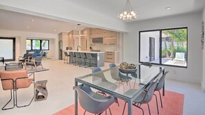 A spacious living area with a glass dining table, modern chairs, and a kitchen in the background. - Luxe Wilton Manors Home w/ Private Boat Dock (Wilton Manors)