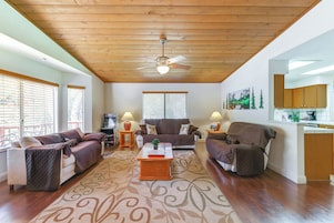 A living room with a ceiling fan, two couches, a coffee table, and a kitchen area with wooden cabinets.