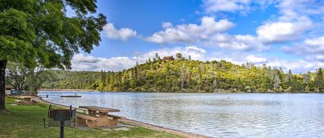 Un parc au bord du lac, doté de tables de pique-nique et d’un banc, entouré d’arbres et bordé d’une colline où se trouvent des bâtiments.
