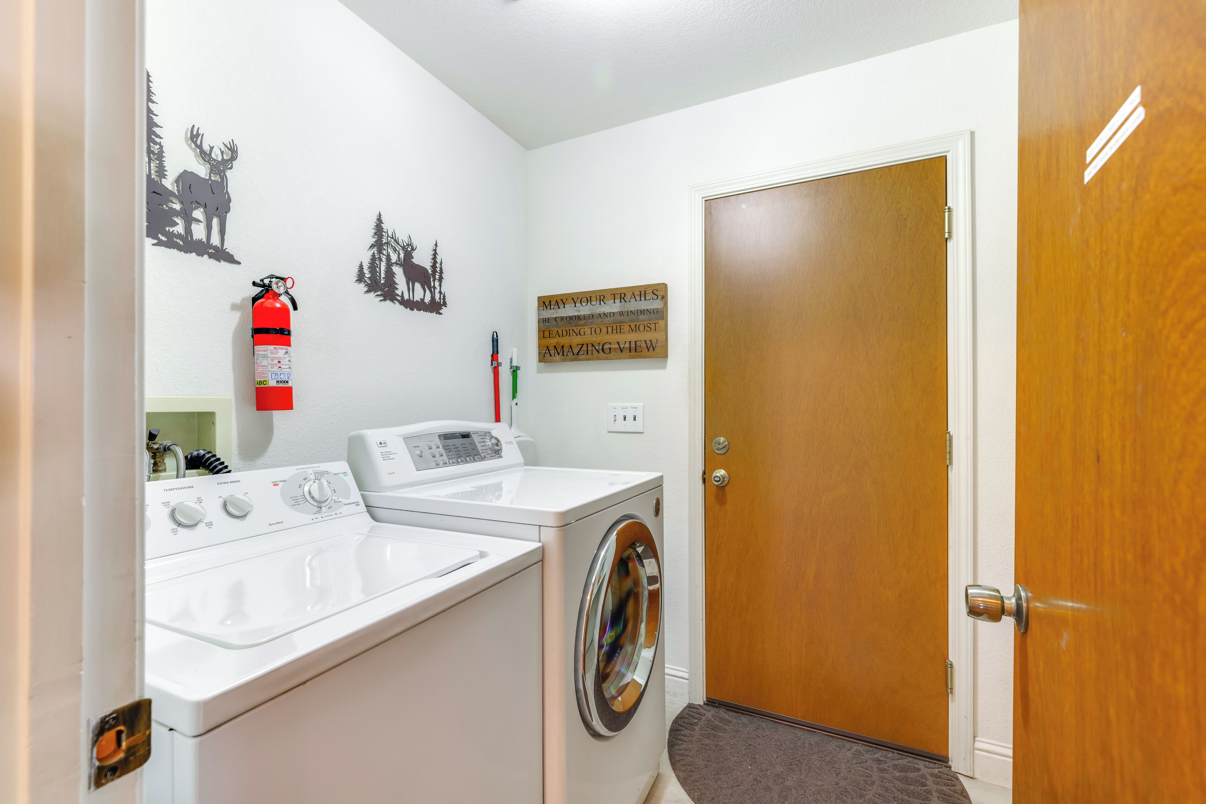 A laundry area with a washing machine and dryer, a fire extinguisher, and a door with a wooden finish.