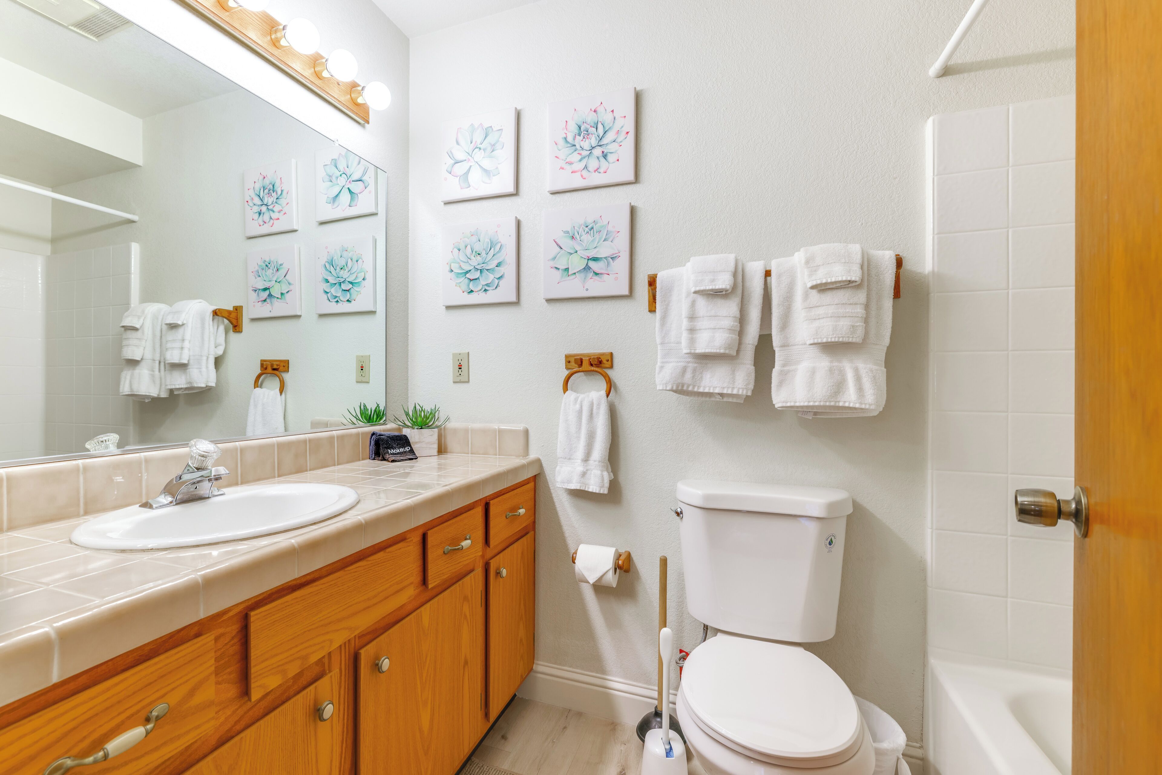 Un bagno moderno con lavandino, toilette e vasca. Diversi asciugamani sono appesi a un porta asciugamani e luci a parete illuminano lo specchio.