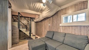 A modern living room with a sectional sofa, a staircase, and a window with a view of trees. - Lakefront Vacation Rental w/ Deck & 2 Docks! (Williford)