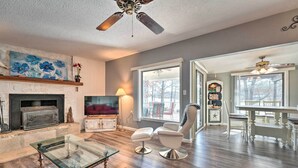 A living room with a fireplace, a glass coffee table, a TV, and a dining area with a table and chairs. - Lakefront Vacation Rental w/ Deck & 2 Docks! (Williford)