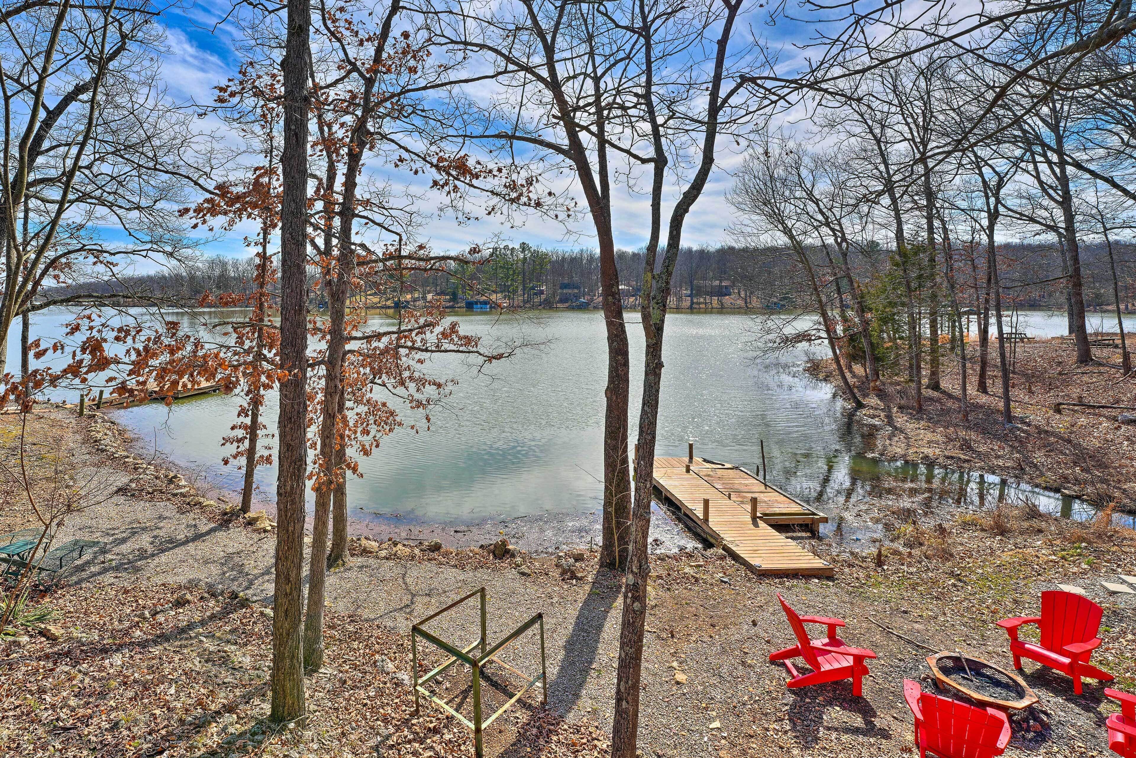 A lakeside view with a dock, red chairs, and a fire pit.