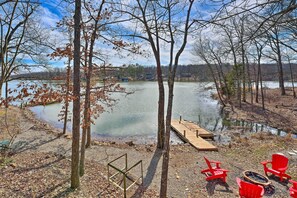 A lakeside view with a dock, red chairs, and a fire pit. - Lakefront Vacation Rental w/ Deck & 2 Docks! (Williford)